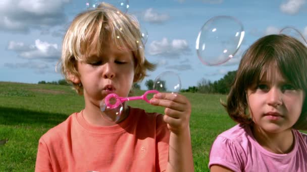 Small boy blowing bubbles with a girl — Stock Video