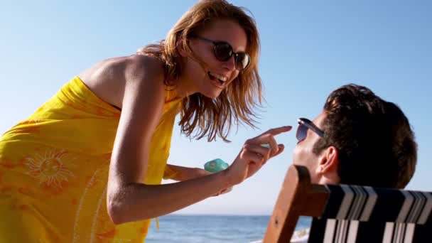 Frau sprüht einem Mann Sonnencreme auf die Nase — Stockvideo