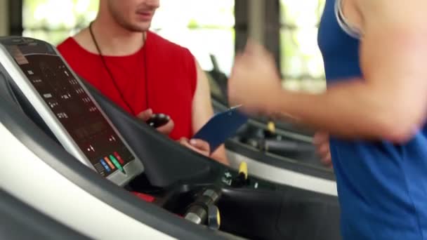 Entrenador masculino escribiendo sobre el rendimiento de la cinta de correr — Vídeos de Stock