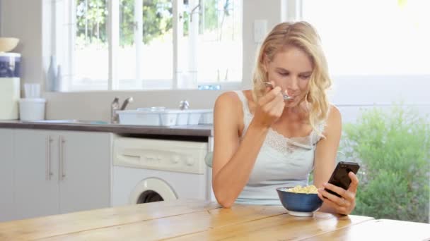 Женщина ест хлопья, глядя на смартфон — стоковое видео