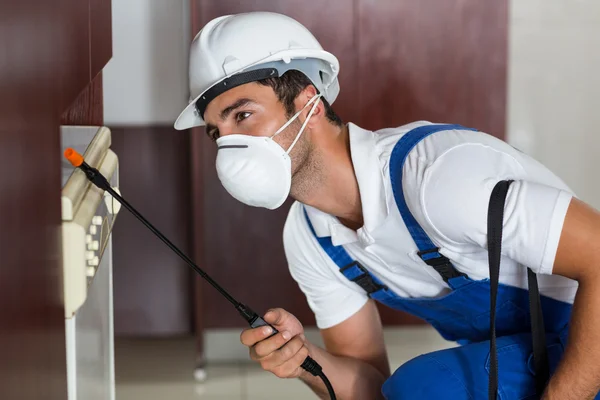 Trabajador de plagas usando pulverizador en gabinetes —  Fotos de Stock