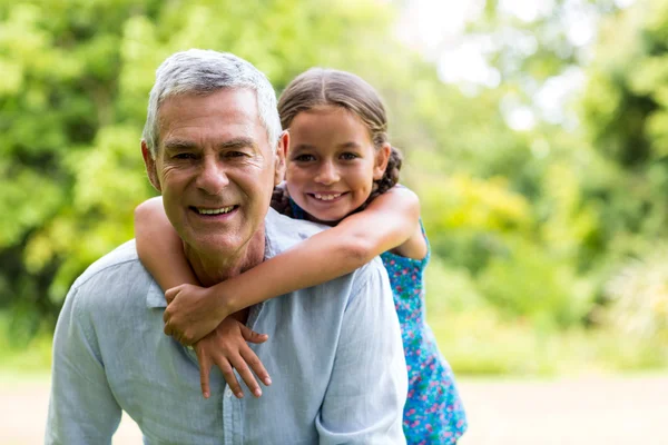 Grandfather carrying grandaughter in yard — Stock Photo, Image