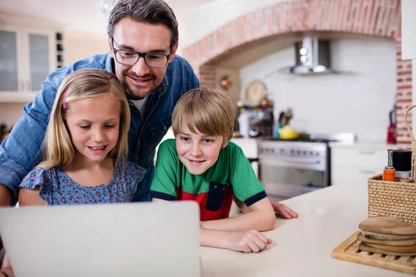 Padre e hijos usando el ordenador portátil en la cocina — Foto de Stock