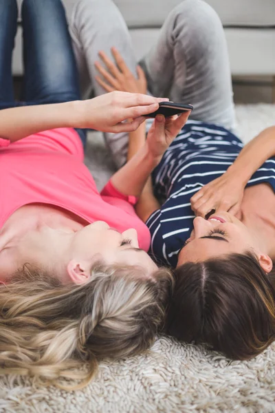 Women lying on rug and looking at phone — Stock Photo, Image