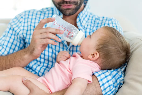 Far utfodring mjölk till son på soffa — Stockfoto