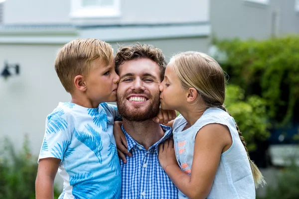 Děti líbání usmívající se otec na dvůr — Stock fotografie