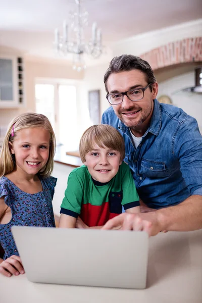 Отец и дети, использующие ноутбук на кухне — стоковое фото