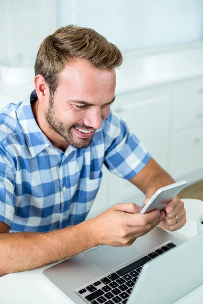 Hombre sonriendo mientras usa el teléfono celular en la cocina —  Fotos de Stock