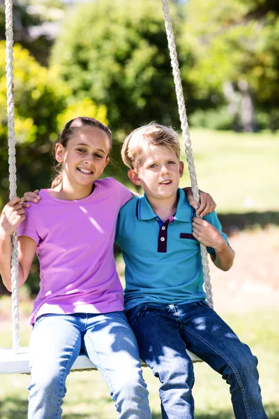 Siblings sitting on swing in park Royalty Free Stock Photos