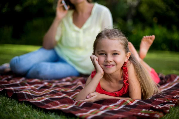 Mädchen liegt auf Decke, während Mutter sitzt — Stockfoto