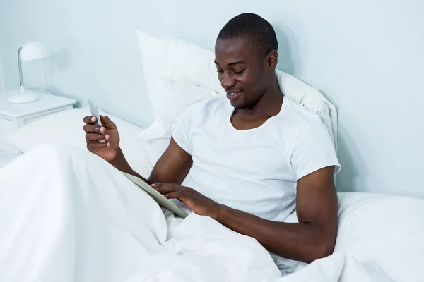 Homem usando tablet e telefone na cama — Fotografia de Stock