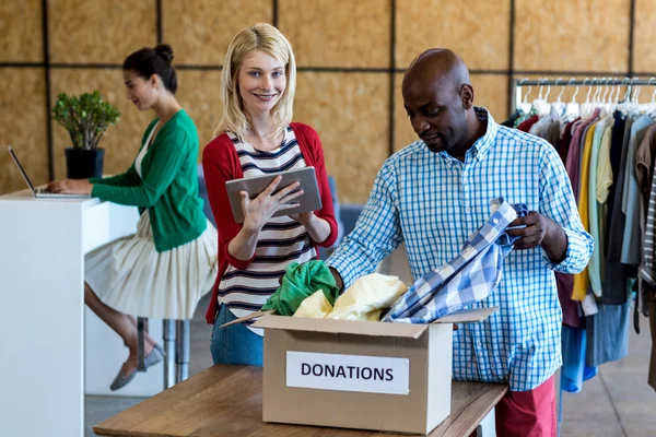 Colegas clasificando la ropa de la caja de donaciones —  Fotos de Stock