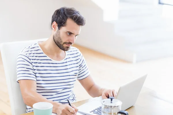 Homem escrevendo nota usando laptop — Fotografia de Stock