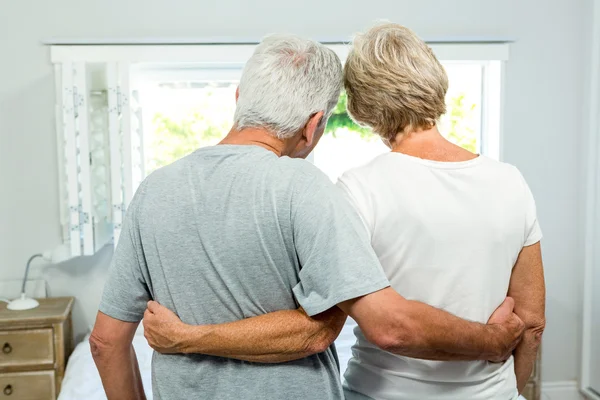 Pareja de ancianos de pie contra ventana — Foto de Stock