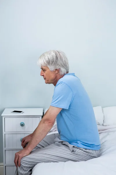 Задумчивый старший мужчина сидит на кровати — стоковое фото