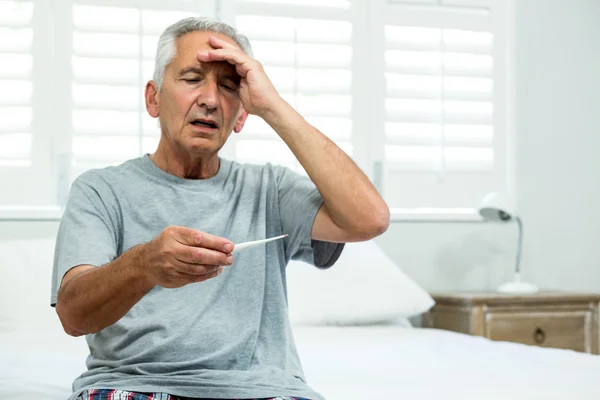 Aged man checking thermometer at home — Stock Photo, Image