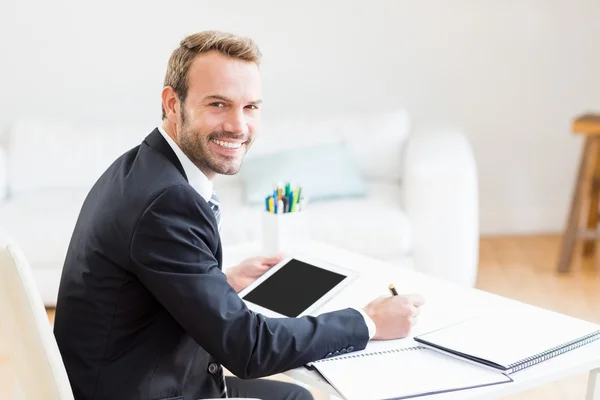 Businessman writing in diary and using tablet — Stock Photo, Image