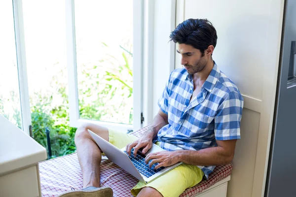 Człowiek siedzi na łóżku za pomocą laptopa — Zdjęcie stockowe