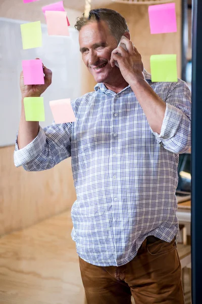 Hombre escribiendo en notas adhesivas mientras habla por teléfono — Foto de Stock