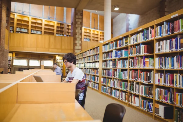 在库中使用他的笔记本电脑的年轻学生 — 图库照片