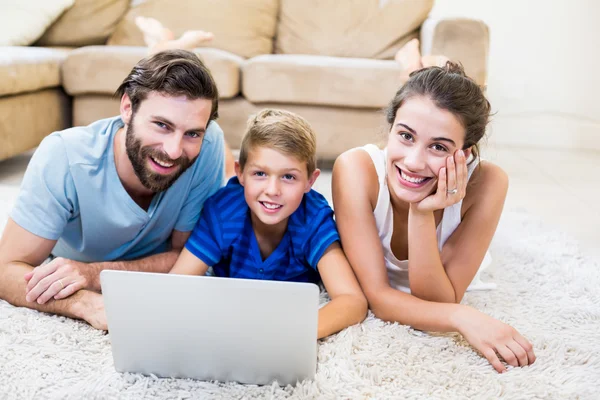 Padres e hijo acostados en la alfombra y el uso de ordenador portátil —  Fotos de Stock