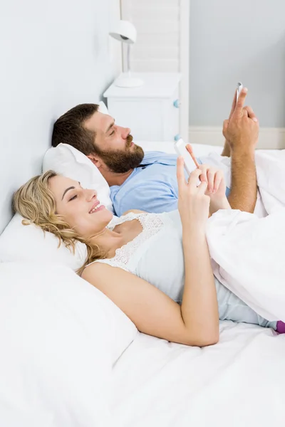 Paar benutzt Handy auf dem Bett — Stockfoto