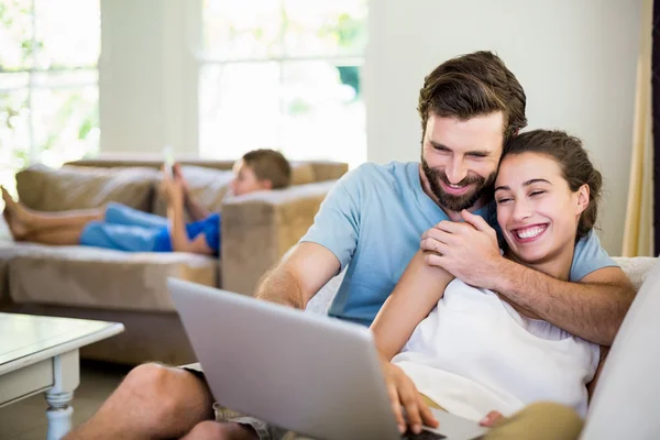 Casal feliz sentado no sofá e usando laptop — Fotografia de Stock