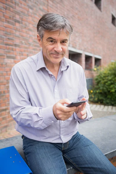 Портрет улыбающегося профессора с помощью мобильного телефона в кампусе — стоковое фото