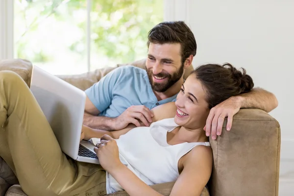 Pareja feliz acostada en el sofá y utilizando el ordenador portátil — Foto de Stock