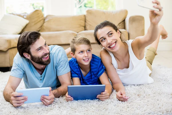 Rodzice i syna leżącego na dywan i selfie biorąc z telefonu — Zdjęcie stockowe