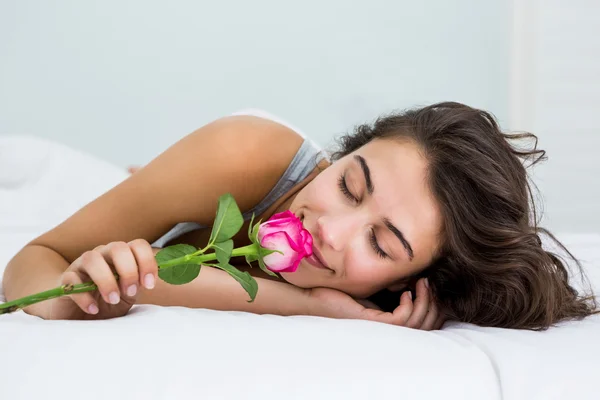 Vrouw ruiken een roze bloem op bed — Stockfoto