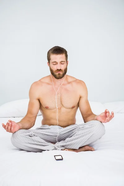 Man doing yoga while listening to music on bed — Stock Photo, Image
