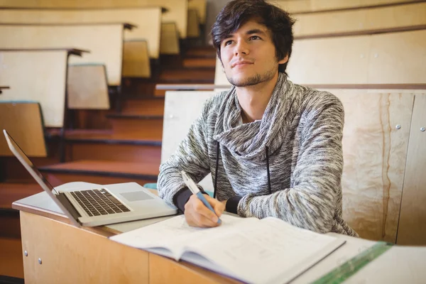 Kitap ve dizüstü bilgisayar ile masa başında oturan düşünceli genç öğrenci — Stok fotoğraf