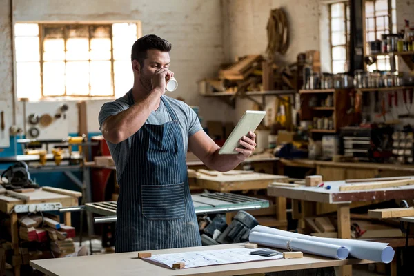 Timmerman met behulp van zijn tablet en het drinken van een kopje koffie — Stockfoto