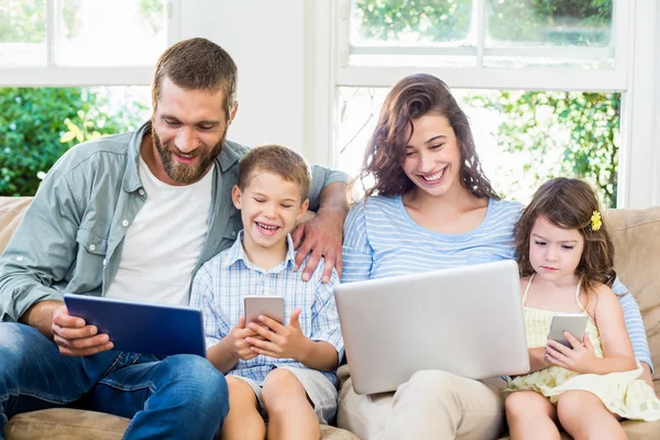 Семья сидит на диване и с помощью ноутбука, планшета и телефона — стоковое фото