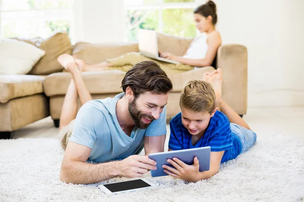 Far och son liggande på matta och använder digital tablet — Stockfoto