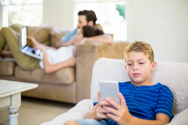 Хлопчик сидить на дивані і використовує мобільний телефон — стокове фото