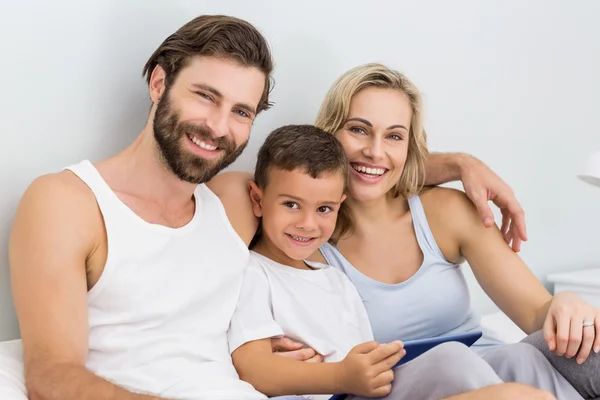 Padres e hijo sentados en la cama y utilizando ficha digital — Foto de Stock