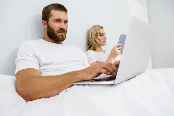 Para za pomocą laptopa i cyfrowe tabletki w łóżku — Zdjęcie stockowe