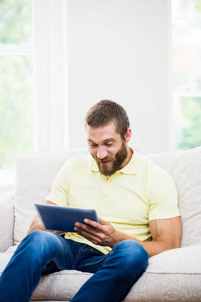 Młody człowiek siedzi na kanapie i za pomocą cyfrowego tabletu — Zdjęcie stockowe