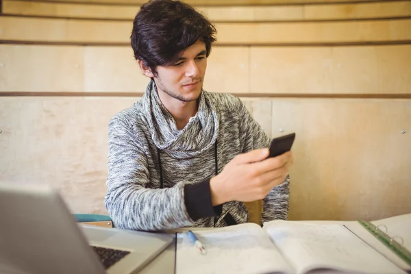 Mladý student sedí u stolu a pomocí mobilního telefonu — Stock fotografie