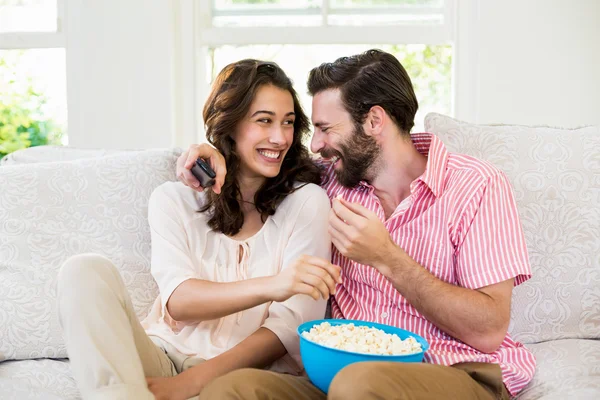 Casal feliz sentado com uma tigela de pipoca no sofá — Fotografia de Stock