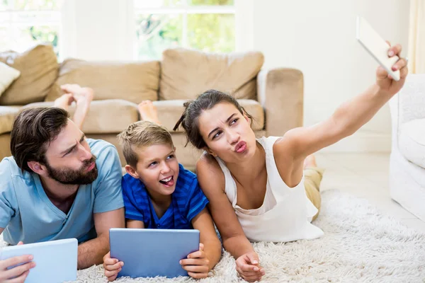 Rodzice i syna leżącego na dywan i selfie biorąc z telefonu — Zdjęcie stockowe
