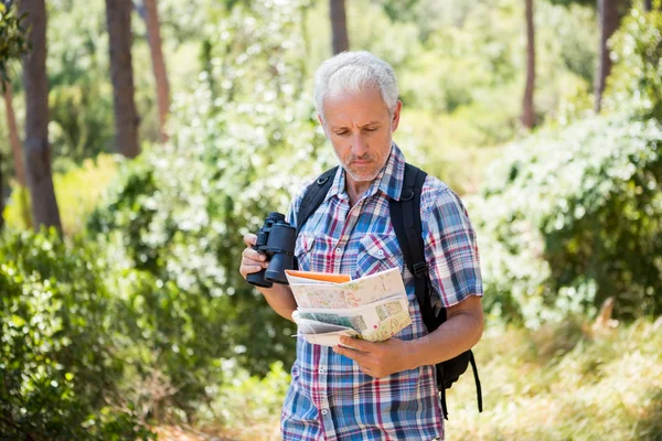 O homem idoso está de pé e carregando um mapa e binóculos — Fotografia de Stock