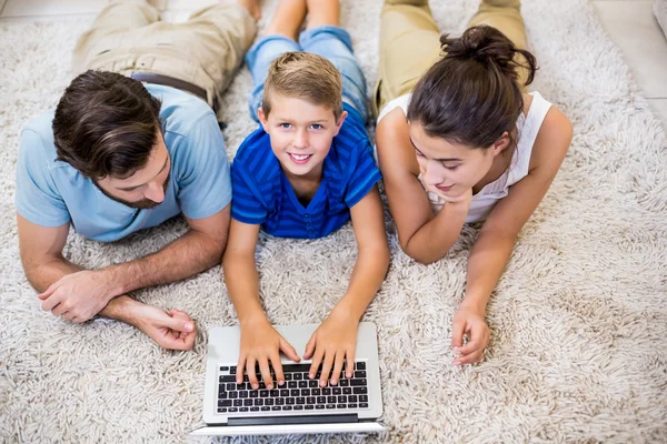 父母和儿子躺在地毯上和使用笔记本电脑 — 图库照片