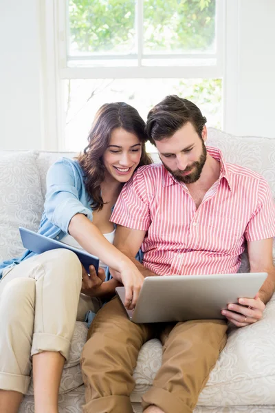 Casal usando tablet digital e laptop na sala de estar — Fotografia de Stock