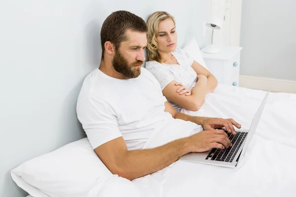 Mujer viendo al hombre mientras usa el portátil en la cama —  Fotos de Stock