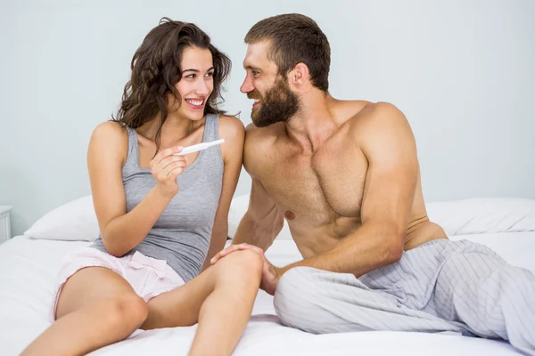 Glückliches Paar schaut sich Schwangerschaftstest im Bett an — Stockfoto