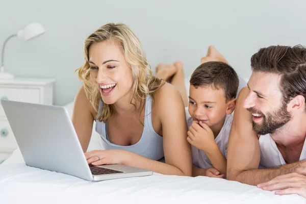 Parents and son lying on bed and using laptop — Stock Photo, Image