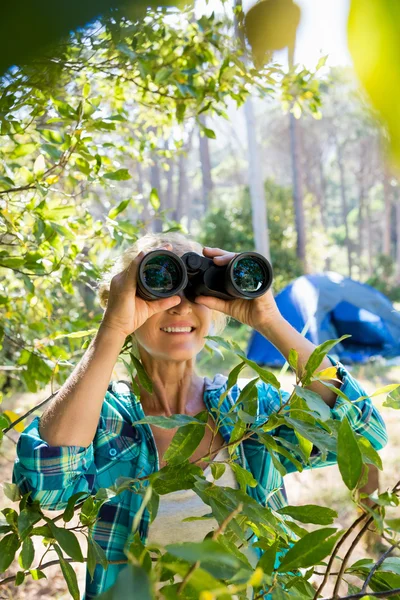 Mature woman smiling and looking on binoculars — Stock Photo, Image